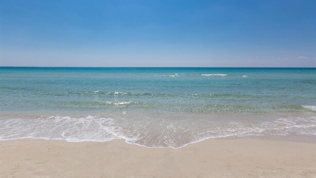 Une plage avec une eau d’un bleu limpide et un rivage sablonneux.