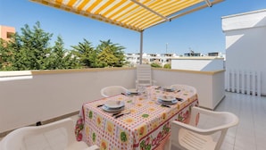 Une terrasse sur le toit, avec une table dressée pour quatre personnes, protégée par un auvent à rayures et entourée de murs blancs et de verdure.