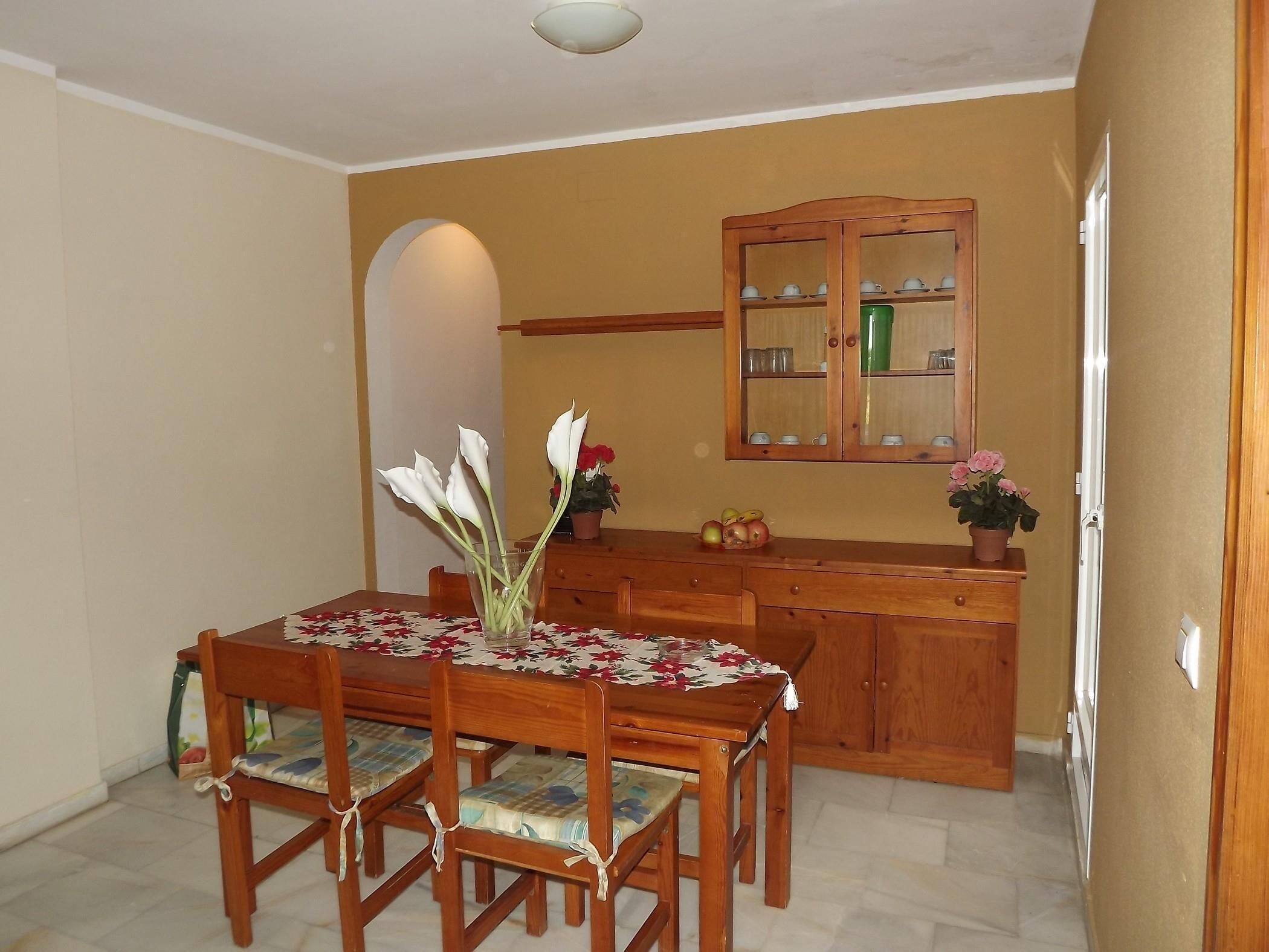 Un coin repas avec une table et des chaises en bois, un buffet aux portes vitrées et un vase rempli de fleurs.