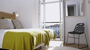 A bedroom with a bed, a green throw, a chair, a balcony, and a window.