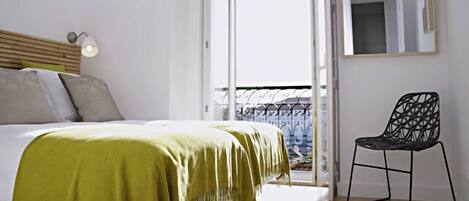 Un dormitorio con cama, una manta verde, una silla, un balcón y una ventana.