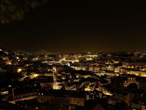 A nighttime view of a densely built urban area with illuminated buildings and a prominent bridge in the background.