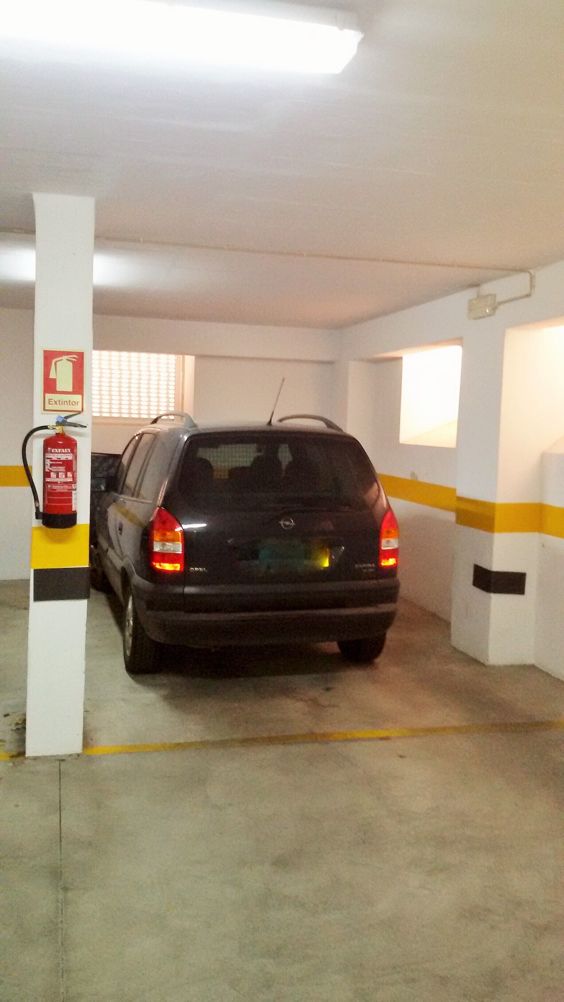 A parking garage with a car parked near a fire extinguisher.