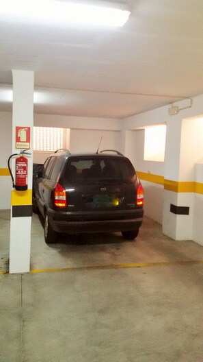 A parking garage with a car parked near a fire extinguisher.
