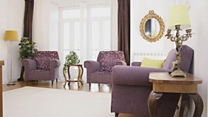 A living room with two purple armchairs, a sofa, a small wooden side table, a floor lamp, a mirror, and a potted plant.