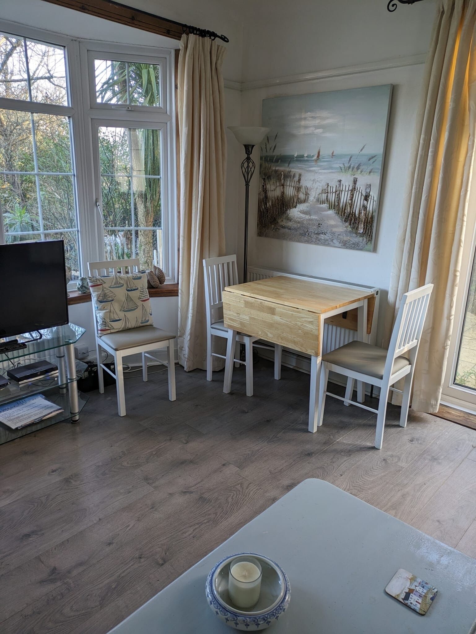 A cozy dining area with a wooden table, white chairs, and a painting of a beach scene.