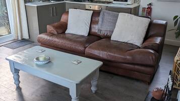 Un accogliente soggiorno con un divano in pelle marrone, un tavolino da caffè bianco e un angolo cottura con elettrodomestici moderni.