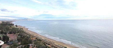 Vista costera con playa, una pequeña masa de agua y un parque con senderos y vegetación.