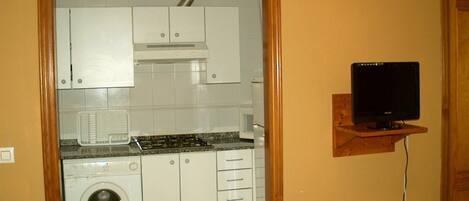 Une cuisine compacte avec des meubles blancs, un lave-linge encastré et un téléviseur à écran plat fixé au mur.