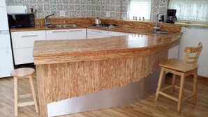 A kitchen with a central island, a sink, a stove, and a microwave. There are two wooden chairs and a small stool. The kitchen has patterned tile backsplash and wooden flooring. - Seolrem 9 (Yangyang)