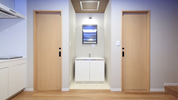 Um corredor com duas portas de madeira, um armário branco com pia e uma luminária no teto.