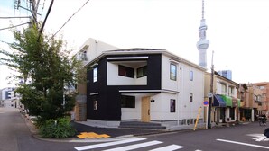 Uma casa moderna de dois andares com fachada preta e branca, entrada visível e vista da rua com faixa de pedestres.