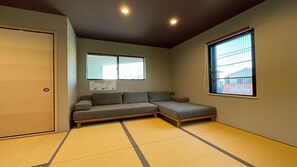 A room with tatami flooring, a sofa, a window with blinds, and a door. - COTO Tokyo Asakusa 5 (Tokyo)