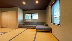 Quarto com tatames, cama de madeira baixa, sofá e uma grande janela com persianas.