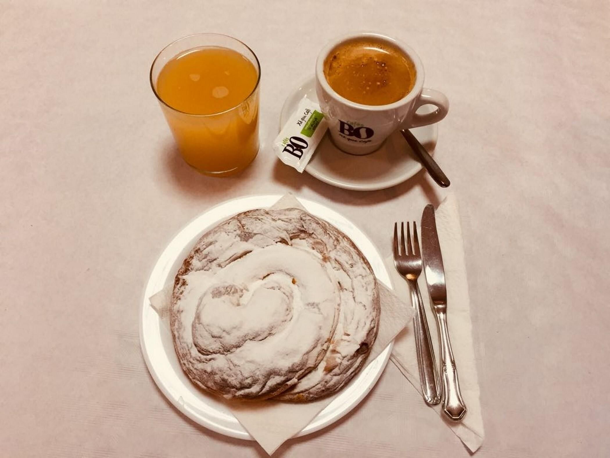 A plate with a pastry, a glass of orange juice, and a cup of coffee on a table.