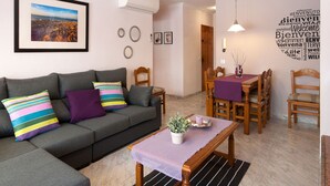 A modern living room with a grey sofa, a wooden dining table with chairs, and a wall with a word cloud. - Obelisc-3, 3 DB ground-floor apartment near the beach. (Can Picafort)