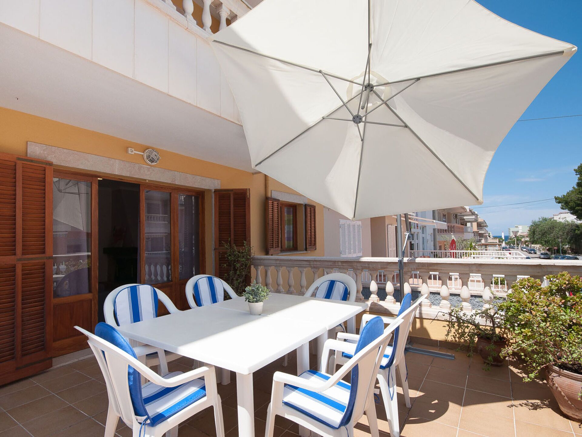 An outdoor patio with a white table and chairs, a large umbrella, and a view of the street.