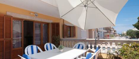 An outdoor patio with a white table and chairs, a large umbrella, and a view of the street.