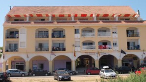 Un immeuble à plusieurs étages, doté d’un toit en tuiles, de nombreux balcons et d’une entrée au niveau du sol portant l’inscription « RESTAURANT ».