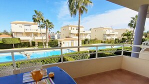 Un balcó amb vista a una piscina, palmeres i edificis al fons.