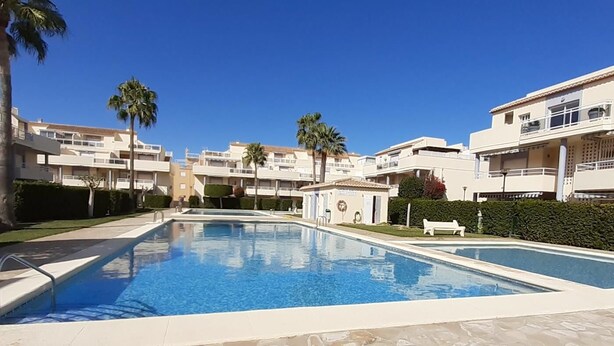 Una piscina envoltada d'edificis d'apartaments moderns, amb palmeres i un cel blau clar.