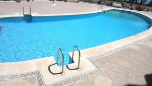 Una piscina de borde curvo, rodeada por una terraza con baldosas y palmeras.