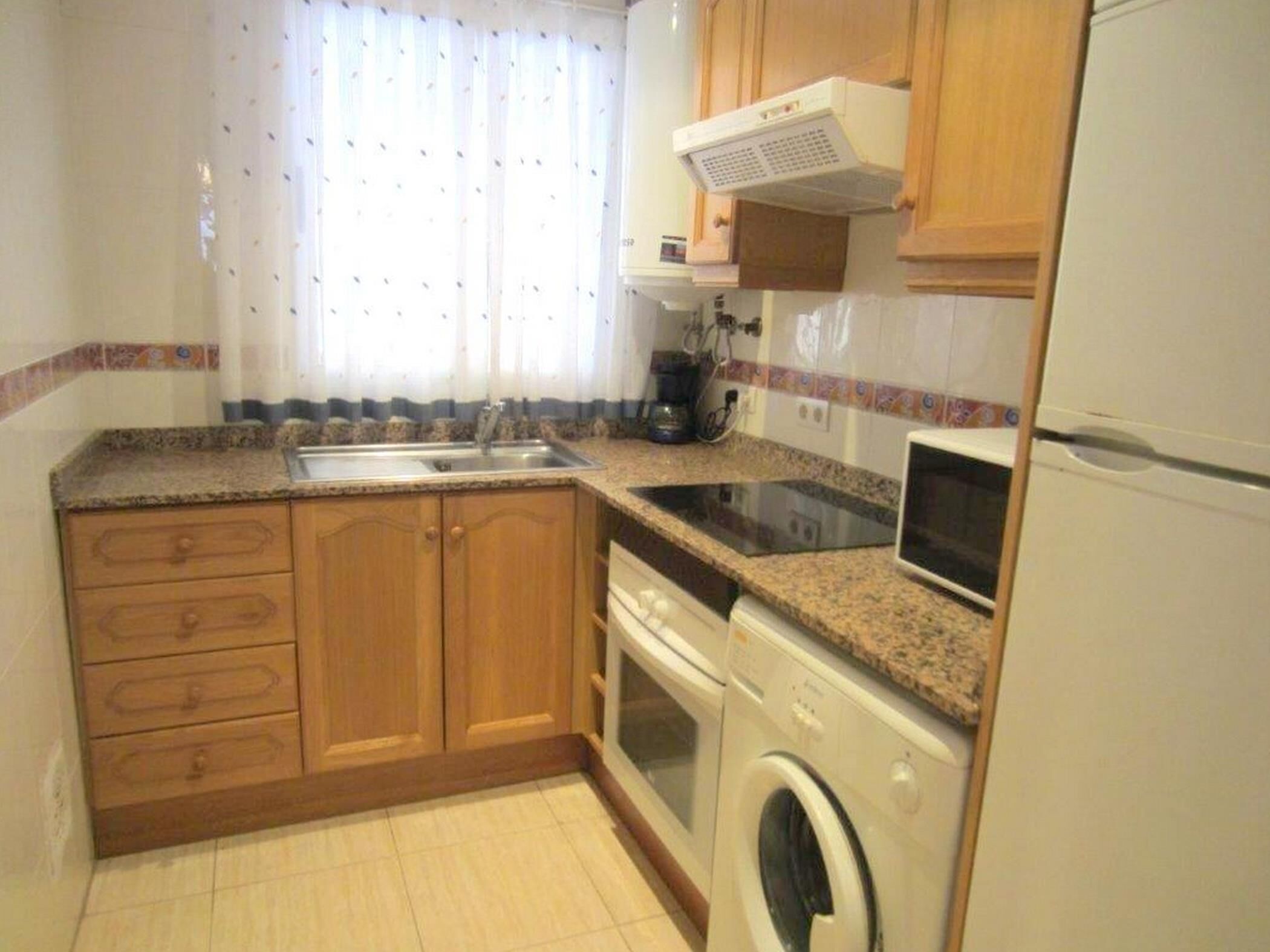 Una cocina con armarios de madera, un lavamanos, una estufa, un microondas y una lavadora.