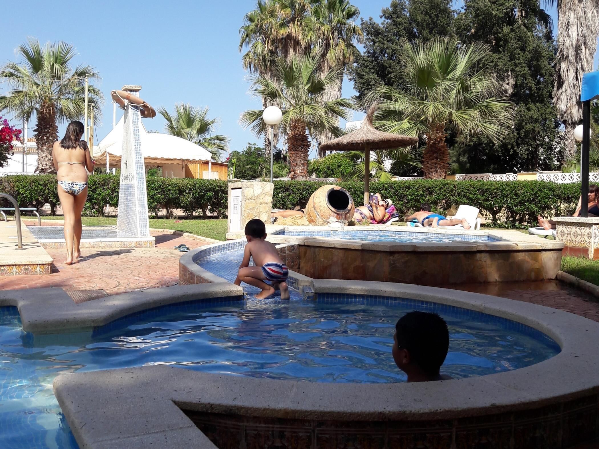 A pool area with a hot tub, lounge chairs, and palm trees.