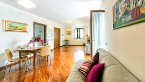 Ein großzügiger Wohnbereich mit Holzboden, einem Esstisch mit Stühlen, einer Couch mit Kissen und einem Gemälde an der Wand.