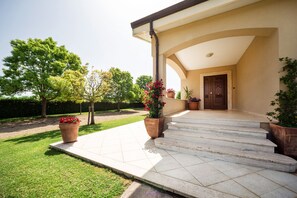 Una casa con porche cubierto, escaleras de piedra y plantas en macetas.