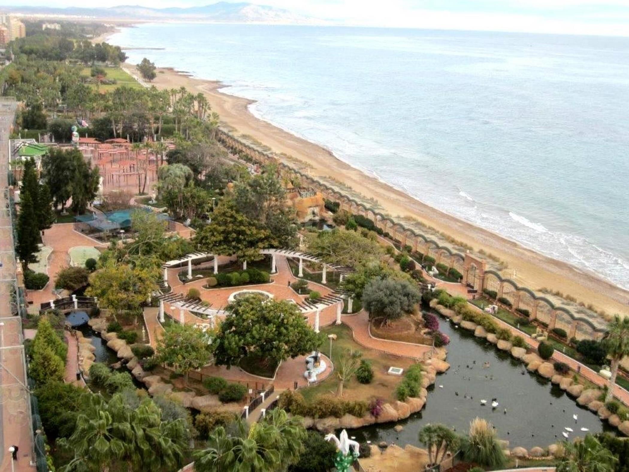 Ein Küstenkurort mit einem zentralen Garten, einer Strandpromenade und Blick auf den Ozean.