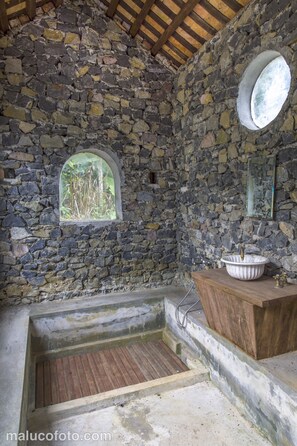 Ein Zimmer mit Stehwänden, einer Holzbadewanne, einem Holzanrichte mit Waschbecken und einem runden Spiegel.
