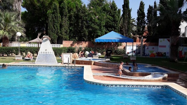 Une piscine avec un toboggan, des chaises longues et un auvent bleu.