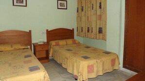 Une chambre avec deux lits simples, une table de chevet, une lampe fixée au mur et une fenêtre avec des rideaux.