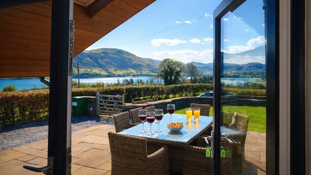 A table with drinks and wicker chairs, overlooking a lake and mountains. - Lake View, luxurious home with 2 ground floor bedrooms, stunning Lake Ullswater views. (Penrith)