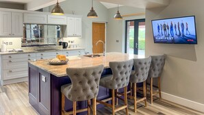 A modern kitchen with white cabinets, a marble countertop, and a large island with bar stools. - Lake View, luxurious home with 2 ground floor bedrooms, stunning Lake Ullswater views. (Penrith)