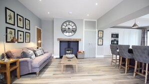 A living room with a sofa, coffee table, fireplace, and dining area with chairs. - Lake View, luxurious home with 2 ground floor bedrooms, stunning Lake Ullswater views. (Penrith)