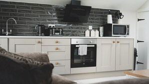 Une cuisine moderne avec un mur de briques noires derrière l’évier, un four encastré, un four à micro-ondes et une machine à café.