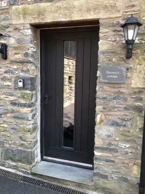 Un edificio de piedra con una puerta negra, una placa con el nombre "Barney's cottage" y una lámpara fijada a la pared.