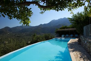 A swimming pool with a view of mountains, surrounded by greenery and stone walls. - Luxury villa overlooking the sea with private pool-Villa Rose (Lefkada)