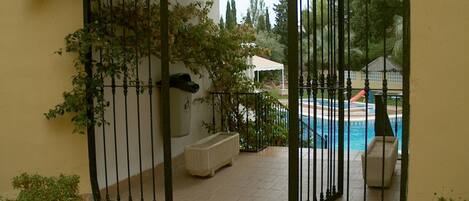 A gated outdoor area with a pool, potted plants, and a white building in the background.