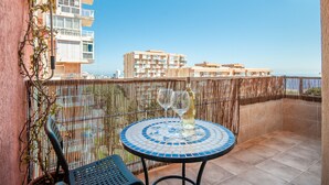 Ein Balkon mit rundem Tisch, zwei Stühlen und einer Weinflasche.