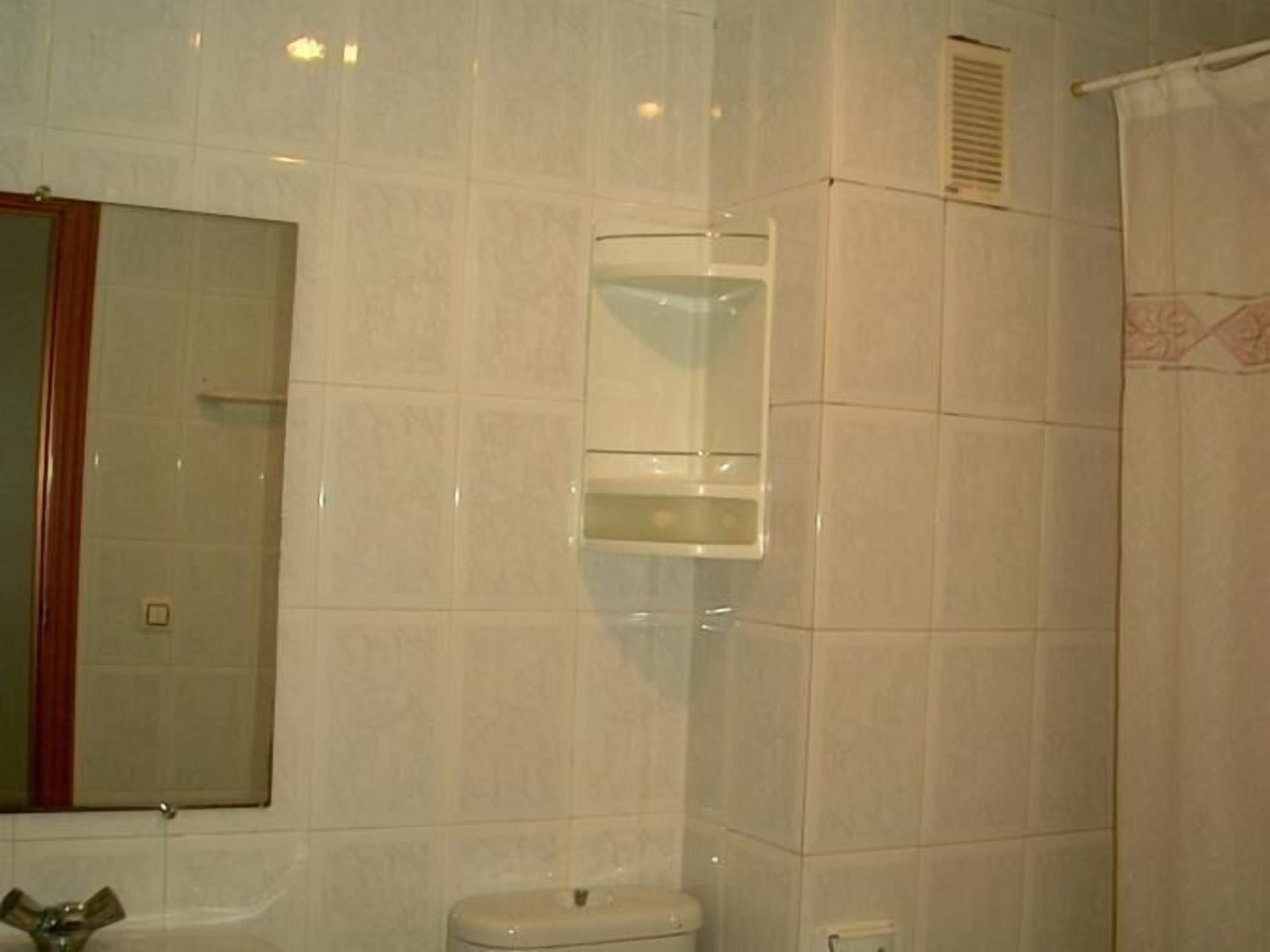 A bathroom with white tiles, a toilet, a sink, and a mirror.