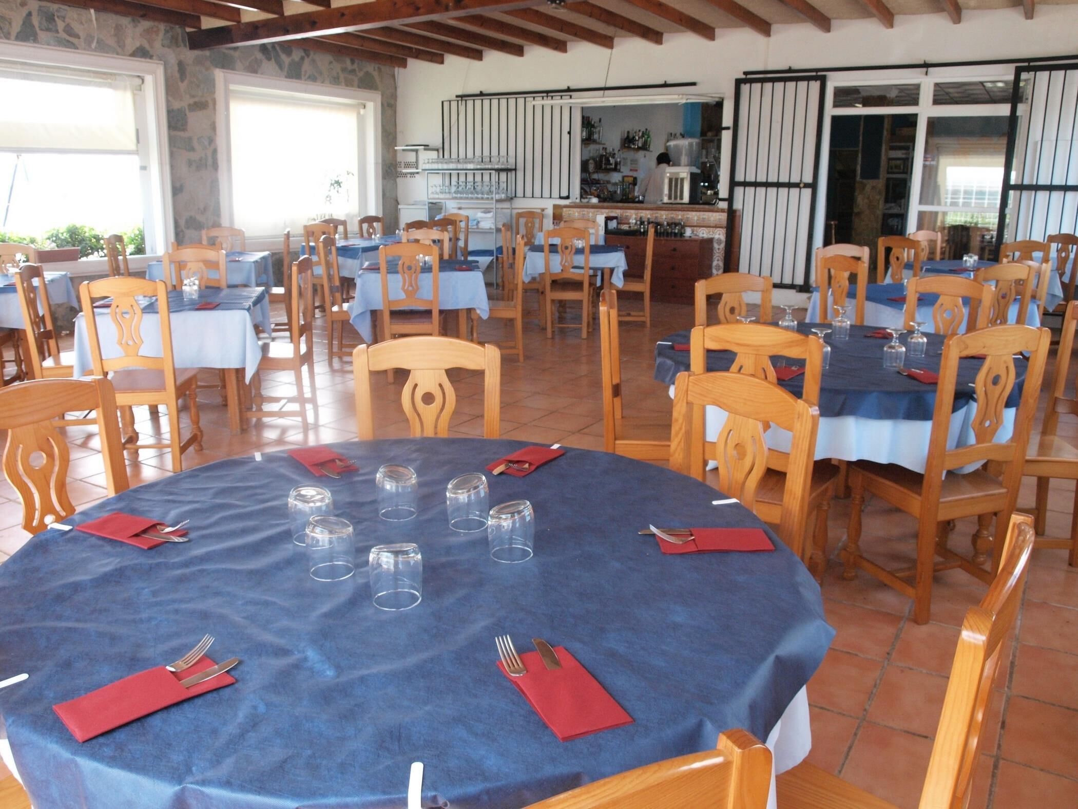 A restaurant with multiple round tables covered with blue tablecloths, wooden chairs, and red napkins.