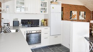 Una cucina compatta con mobili bianchi, forno integrato, frigorifero e macchina del caffè.
