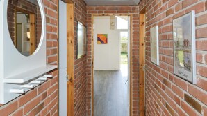 Un corridoio stretto con pareti in mattoni, porte in legno e una porta bianca in fondo che dà sull'esterno.