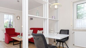 A modern living room with a white sofa, a red armchair, a dining table with chairs, and a bookshelf. - Sandpiper - Haus Andreesen (Neuharlingersiel)