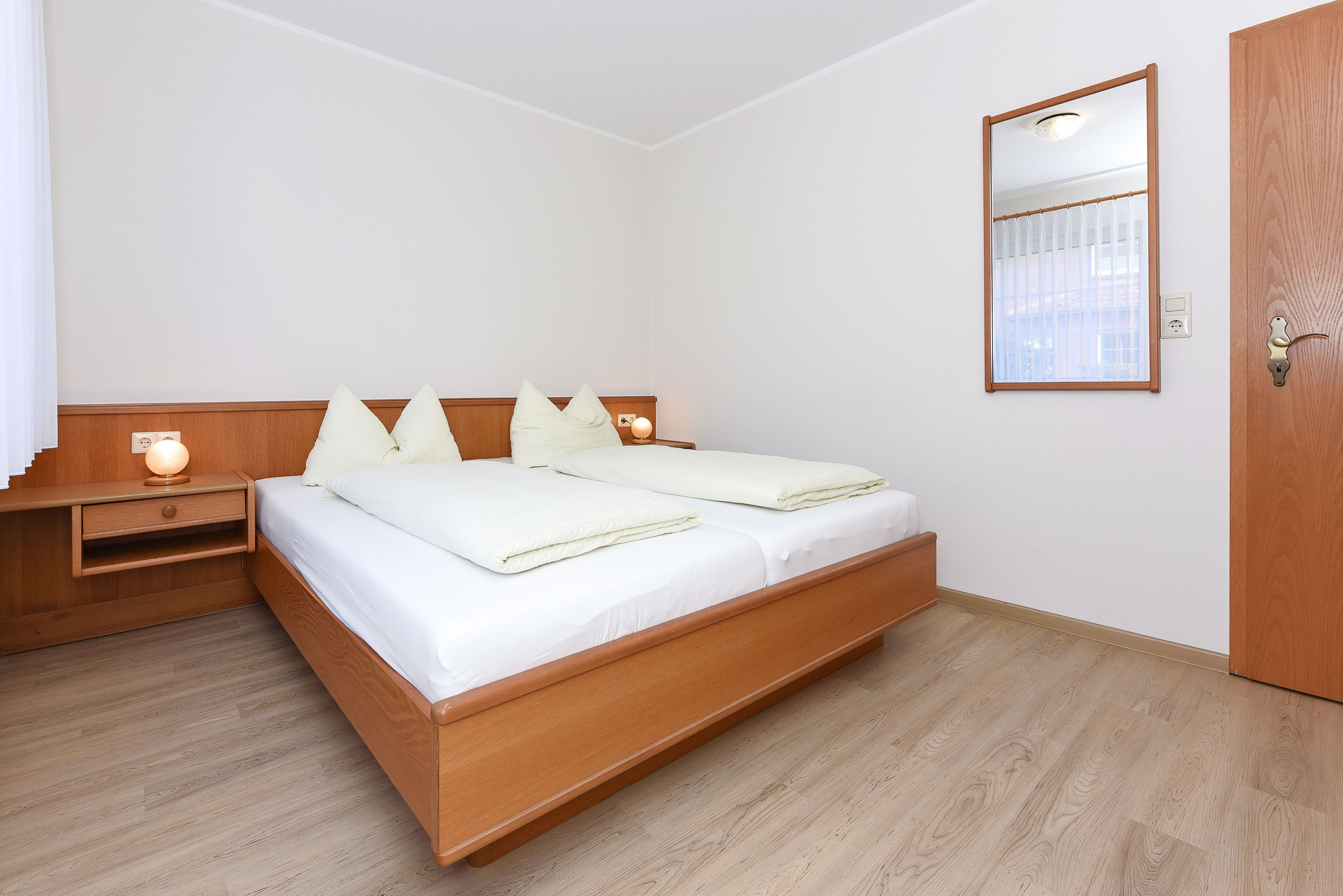 Ein Schlafzimmer mit einem hölzernen Bett, Nachttischen, einem Spiegel und einer Tür.