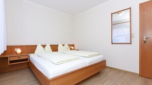 A bedroom with a wooden bed, bedside tables, a nightstand, a mirror, and a door. - Sandpiper - Haus Andreesen (Neuharlingersiel)