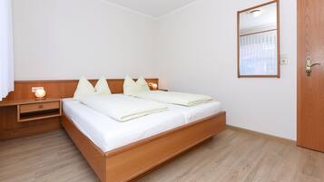Ein Schlafzimmer mit einem hölzernen Bett, Nachttischen, einem Spiegel und einer Tür.